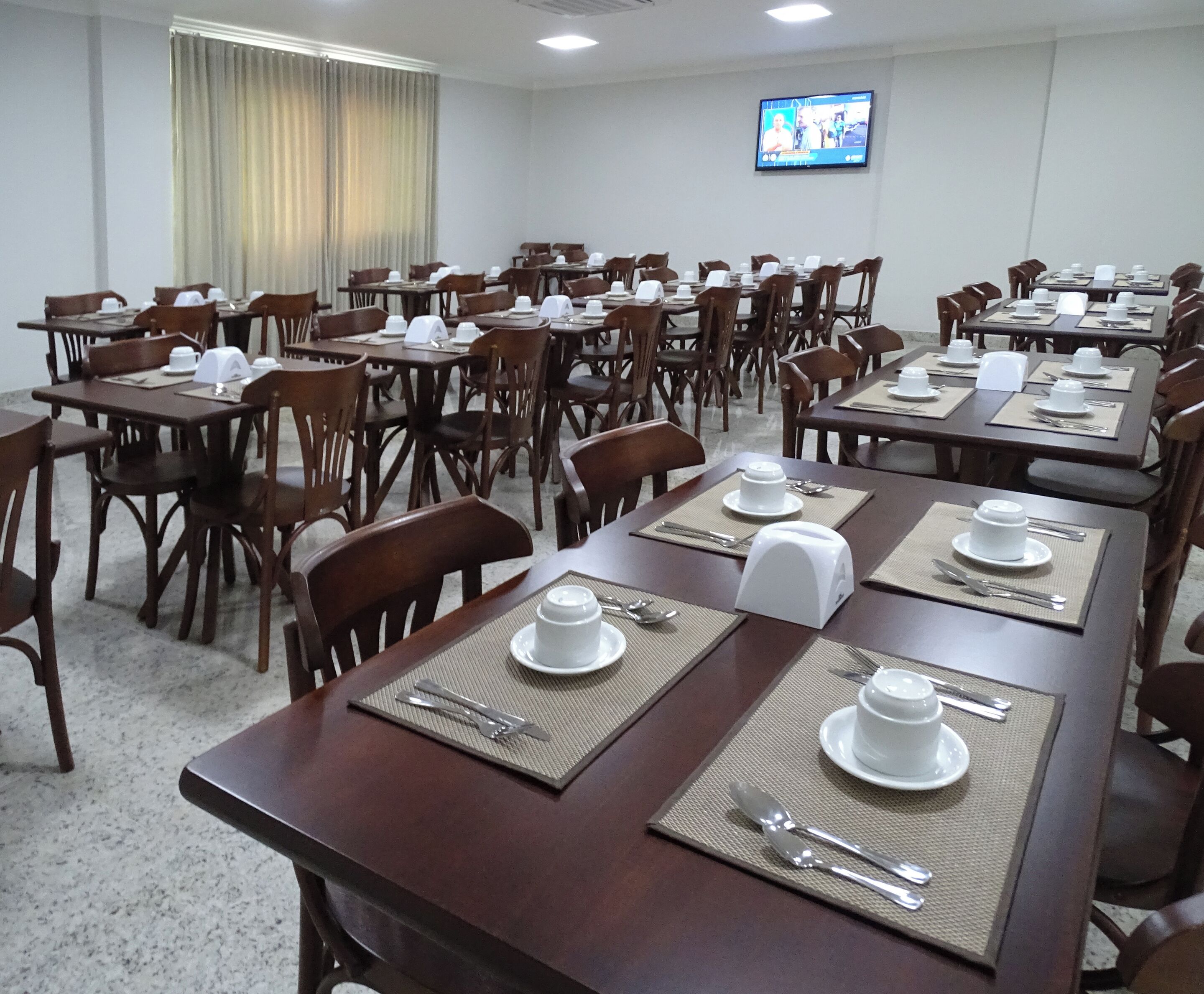 Un salón de conferencias con varias mesas dispuestas para comer, equipado con platos, cubiertos y servilletas.