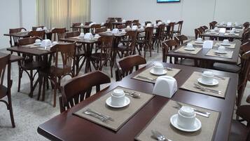 Un salón de conferencias con varias mesas dispuestas para comer, equipado con platos, cubiertos y servilletas.