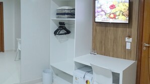 Una habitación pequeña y limpia con un escritorio blanco, una silla y un televisor montado en la pared.