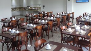 Comedor con varias mesas dispuestas para el servicio, provisto de vajilla y sillas.