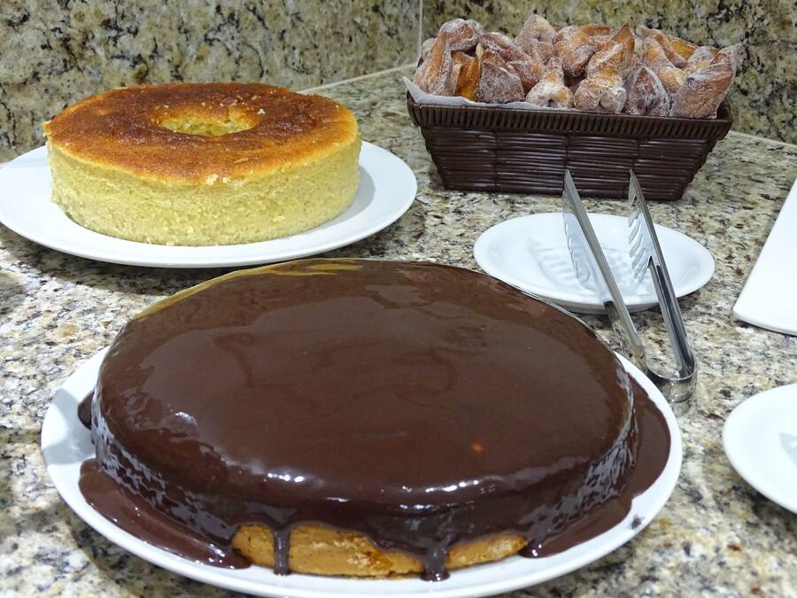 Un pastel con glaseado de chocolate, un pastel redondo sobre un plato, y una cesta de pasteles en una encimera de granito.