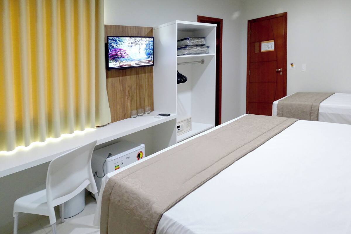 A hotel room with a bed, a desk with a computer, a TV, a wardrobe, and a door.