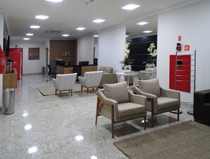 Un vestíbulo moderno con zonas de estar, un mostrador de recepción y un espejo que refleja el espacio.