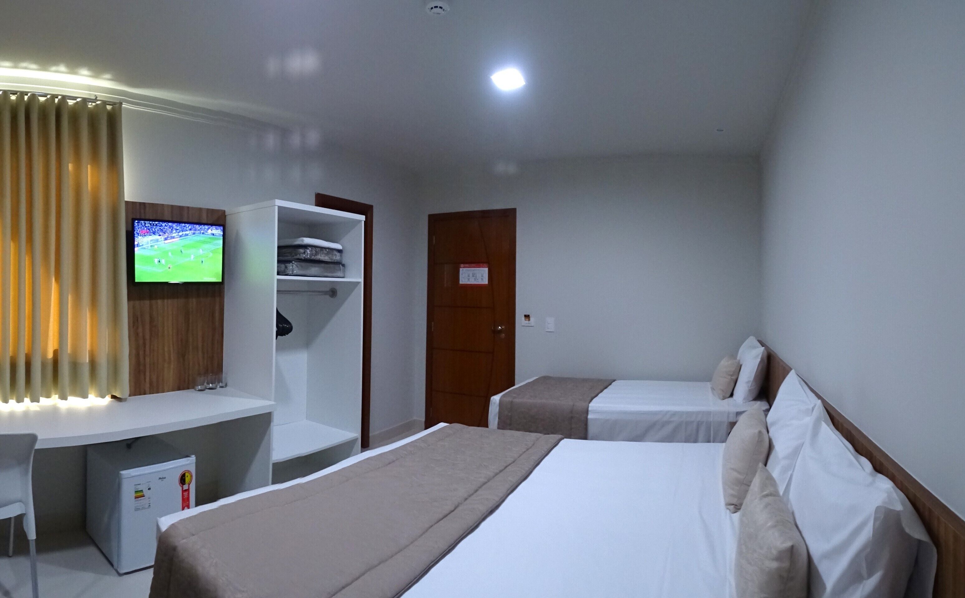 Habitación de hotel con cama, escritorio, televisor, armario y refrigerador pequeño.