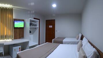 Habitación de hotel con cama, escritorio, televisor, armario y refrigerador pequeño.