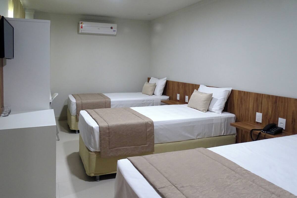 A hotel room with three beds, a desk, and a telephone.