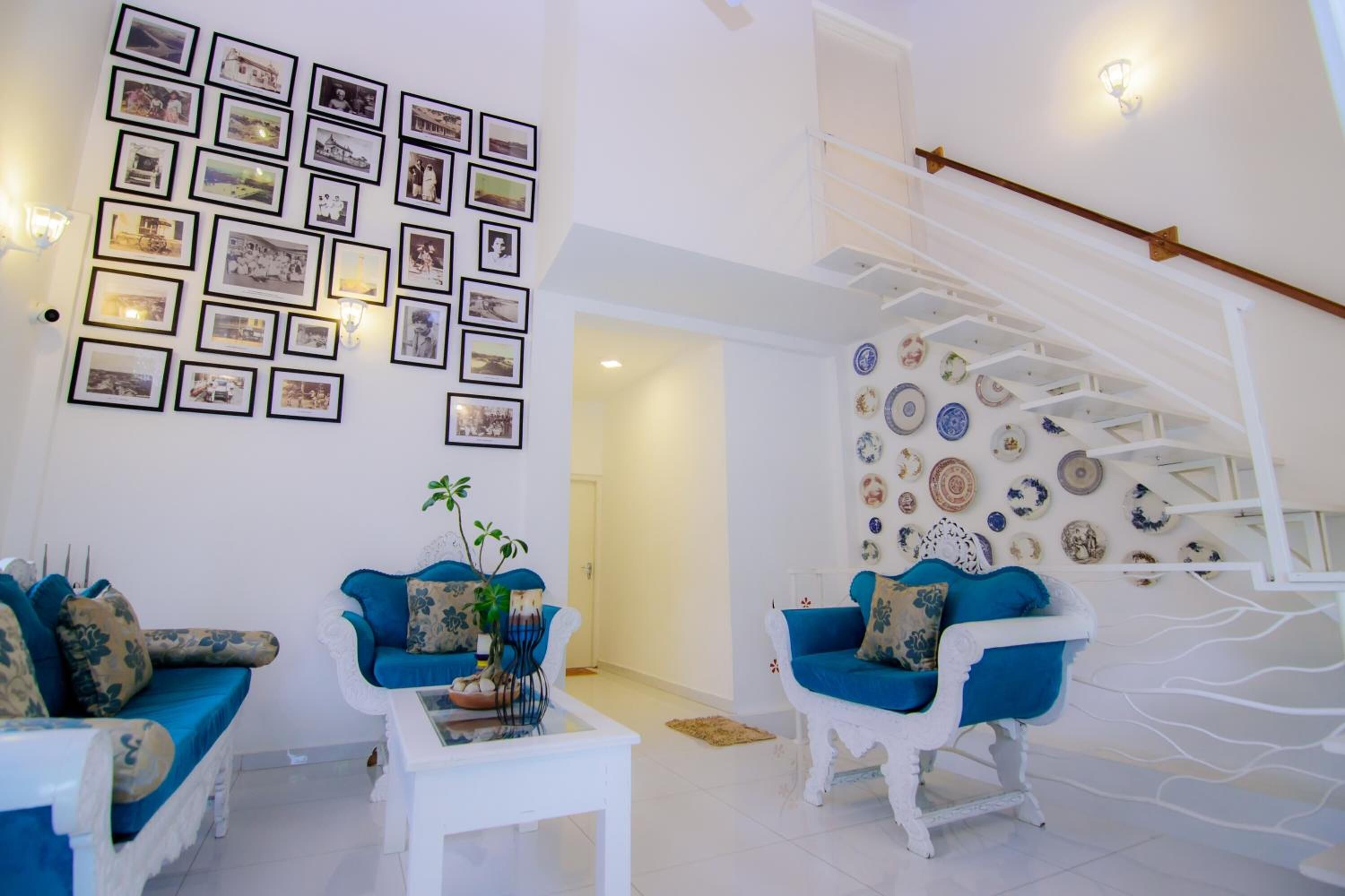 Un vaste salon agrémenté d’un escalier blanc, de canapés bleus et d’un mur décoré de photographies encadrées.