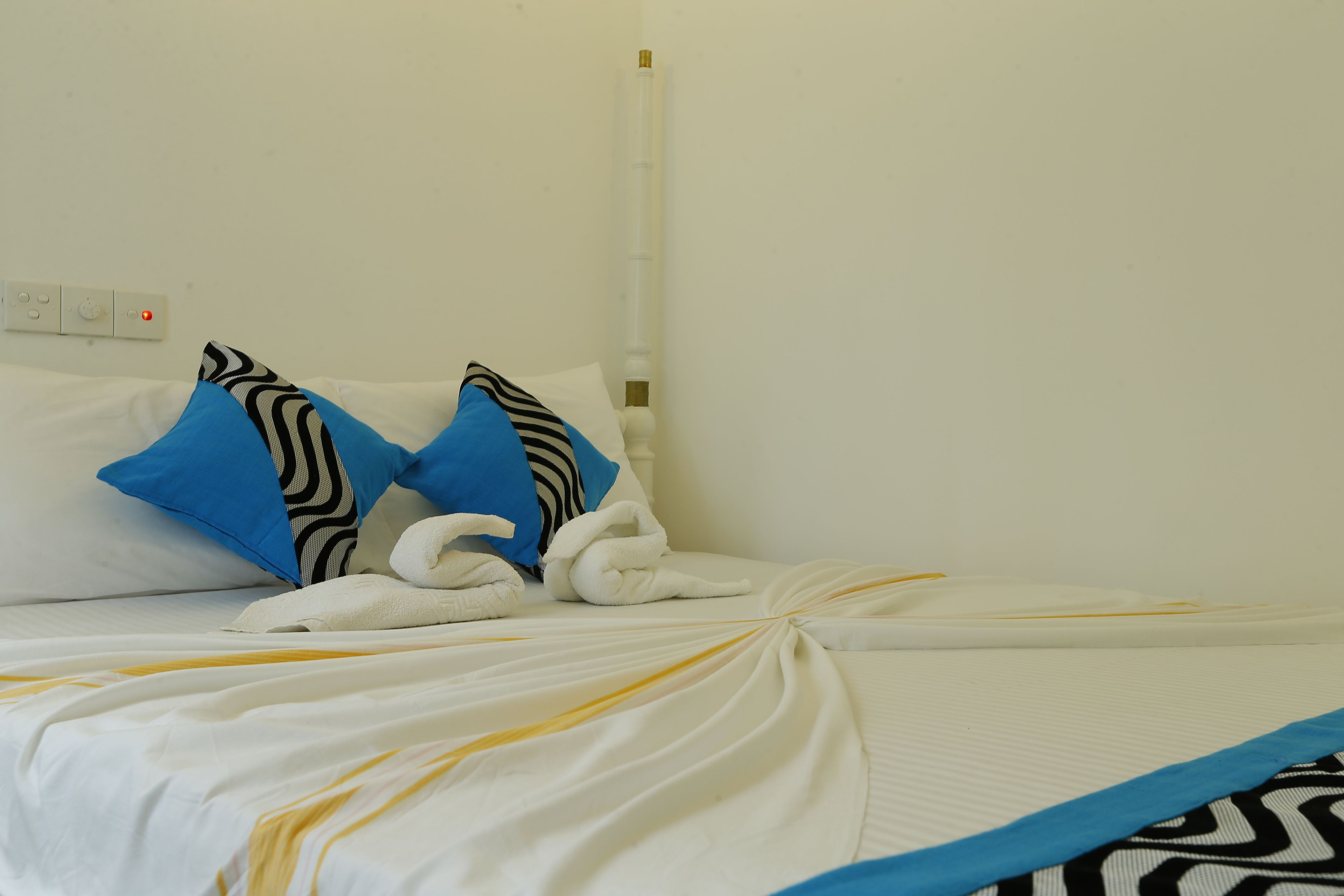 A neatly made bed with white bedding, blue pillows, and a striped pillow.