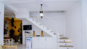 A modern interior with a white staircase, a flat-screen TV, and a kitchen area. - Fort Heaven (Galle)