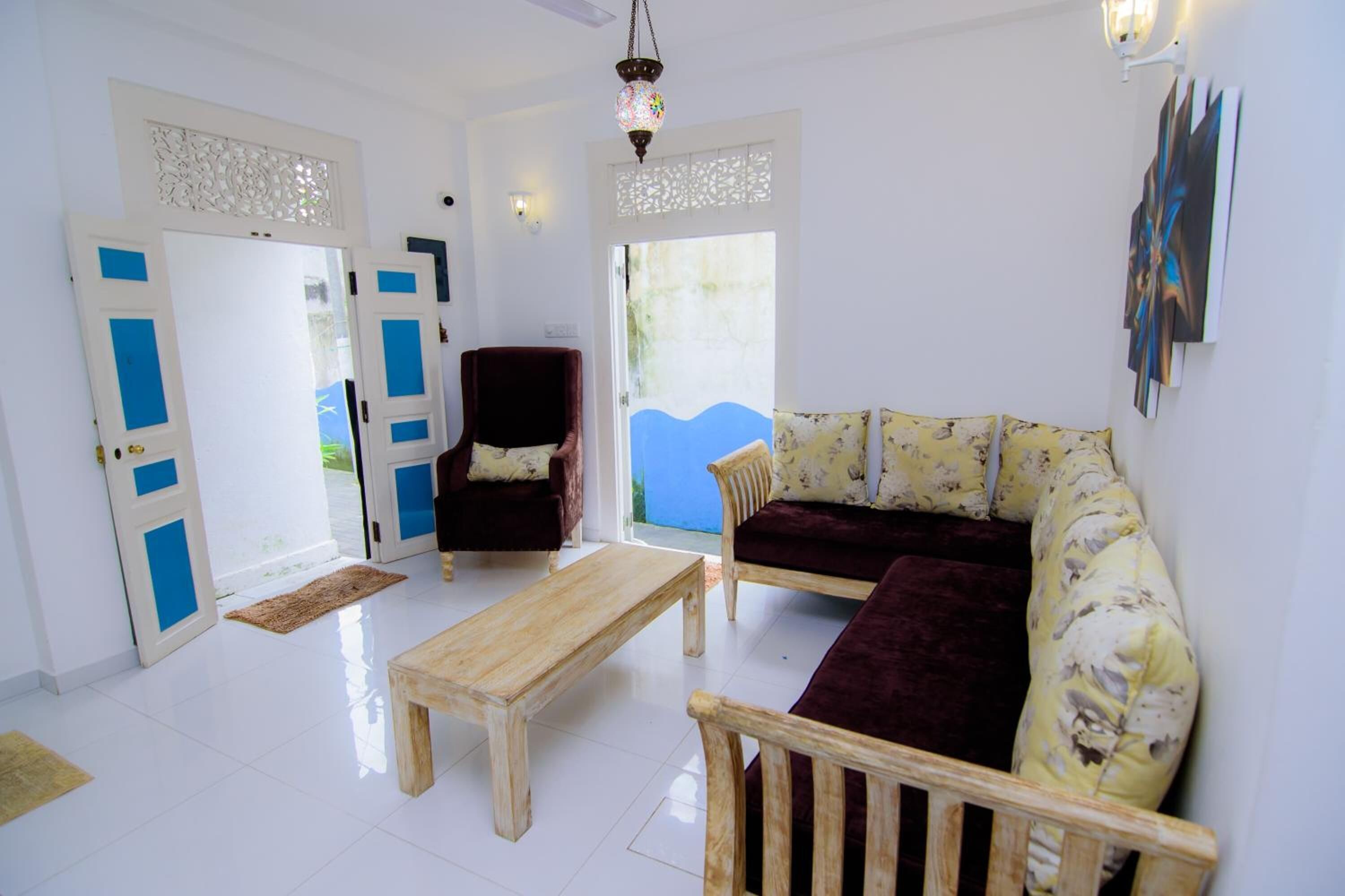 Una sala de estar con una mesa de centro de madera, dos sofás, una silla y una puerta con detalles azules.