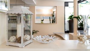 Un espacio interior bien iluminado con un farol decorativo, un arreglo floral de papel blanco y un florero de vidrio con flores secas sobre una mesa.