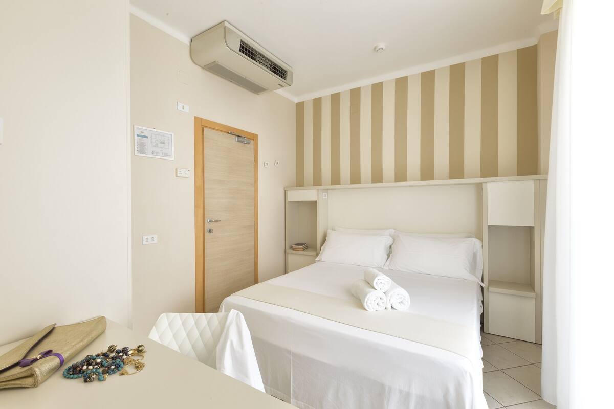 Habitación de hotel con una cama, una mesita de noche, una silla, un armario y una pared a rayas.