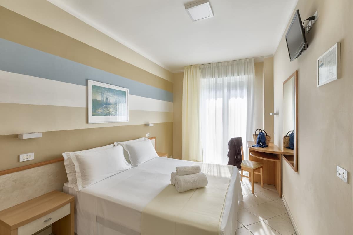 Una habitación de hotel con cama, mesita de noche, escritorio, silla y televisor montado en la pared.
