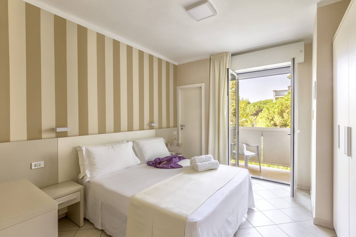 Habitación de hotel con cama, mesita de noche, ventana con cortinas y vistas al exterior.
