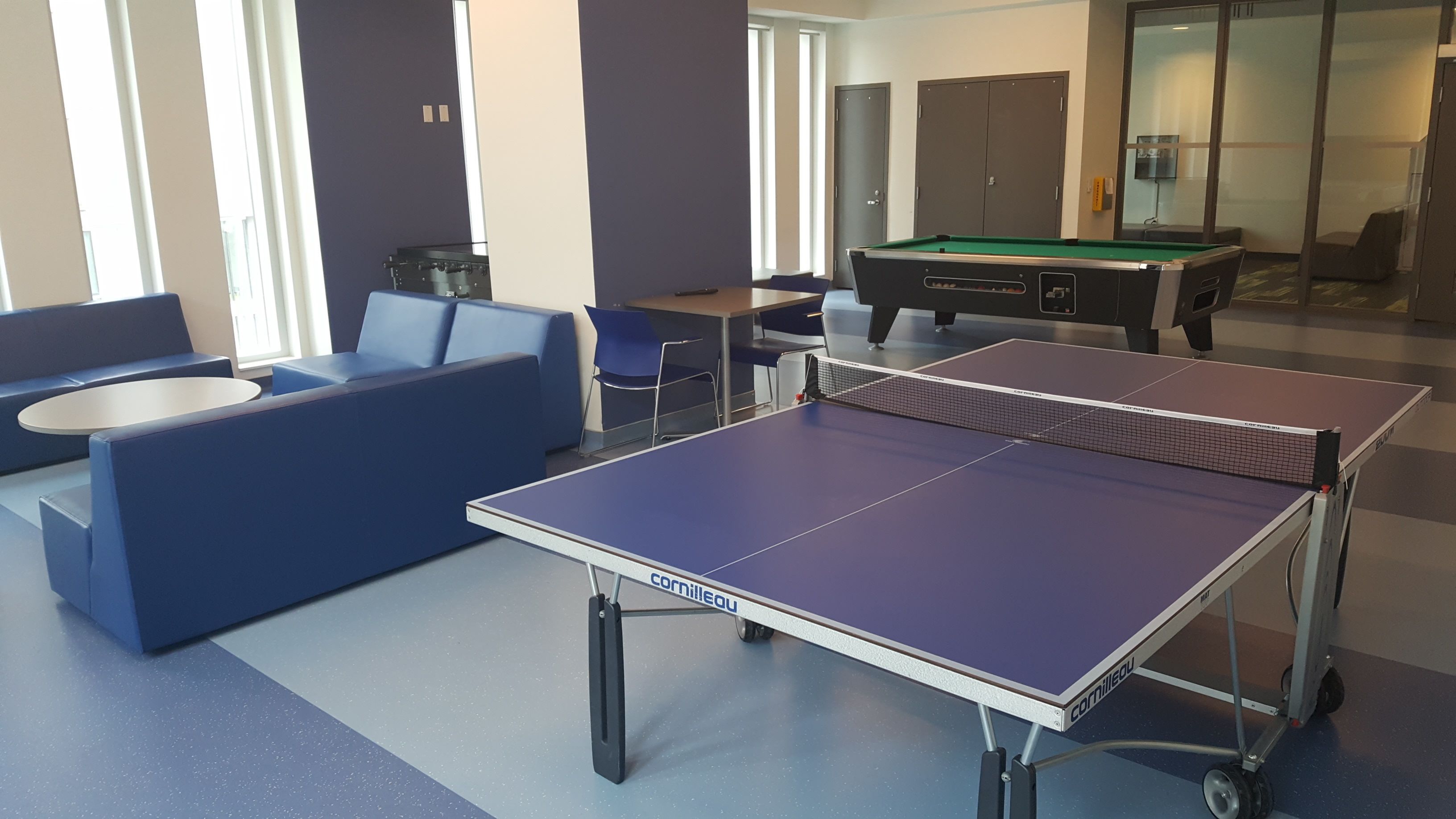 Une pièce équipée d’une table de billard, d’une table de ping-pong et d’un coin salon avec des canapés bleus et une petite table ronde.