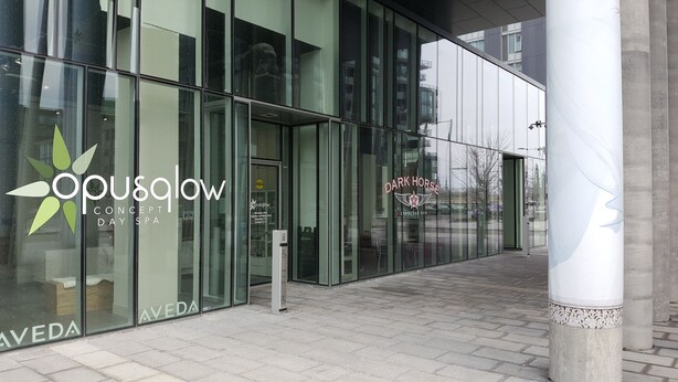 Un edificio moderno con facciate in vetro, un ingresso ben visibile e la segnaletica per 'OPUSglow CONCEPT SPA' e 'DARK HORSE ESPRESSO BAR'.