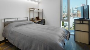Camera d'albergo con un letto, una scrivania, una sedia, una TV e un'ampia finestra vista città.