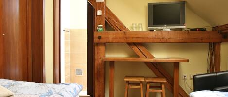 Ein Zimmer mit einem hölzernen Bett, einem kleinen Holztisch, einem Fernseher auf einer Holzablage und einem durchgegangenen Tür erkennbaren Badezimmer.
