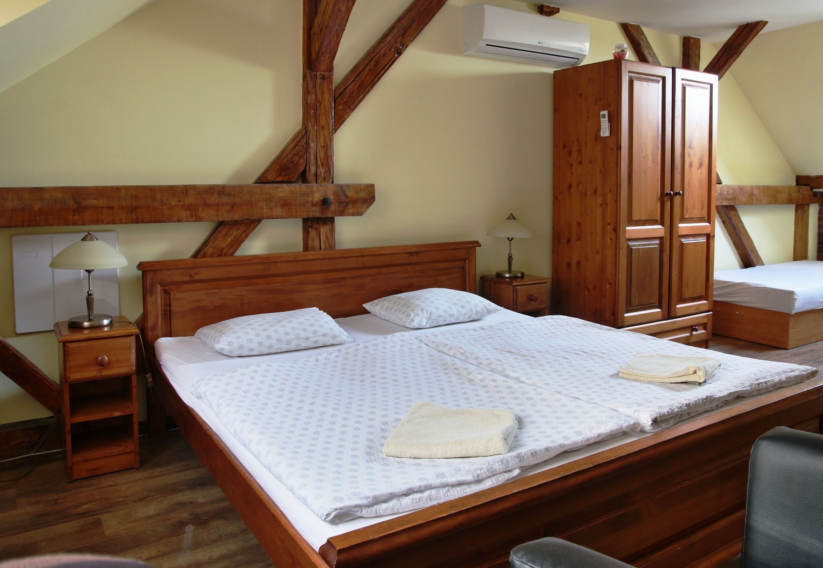 Un dormitorio con una cama de madera, dos mesitas de noche, un armario y un equipo de aire acondicionado.