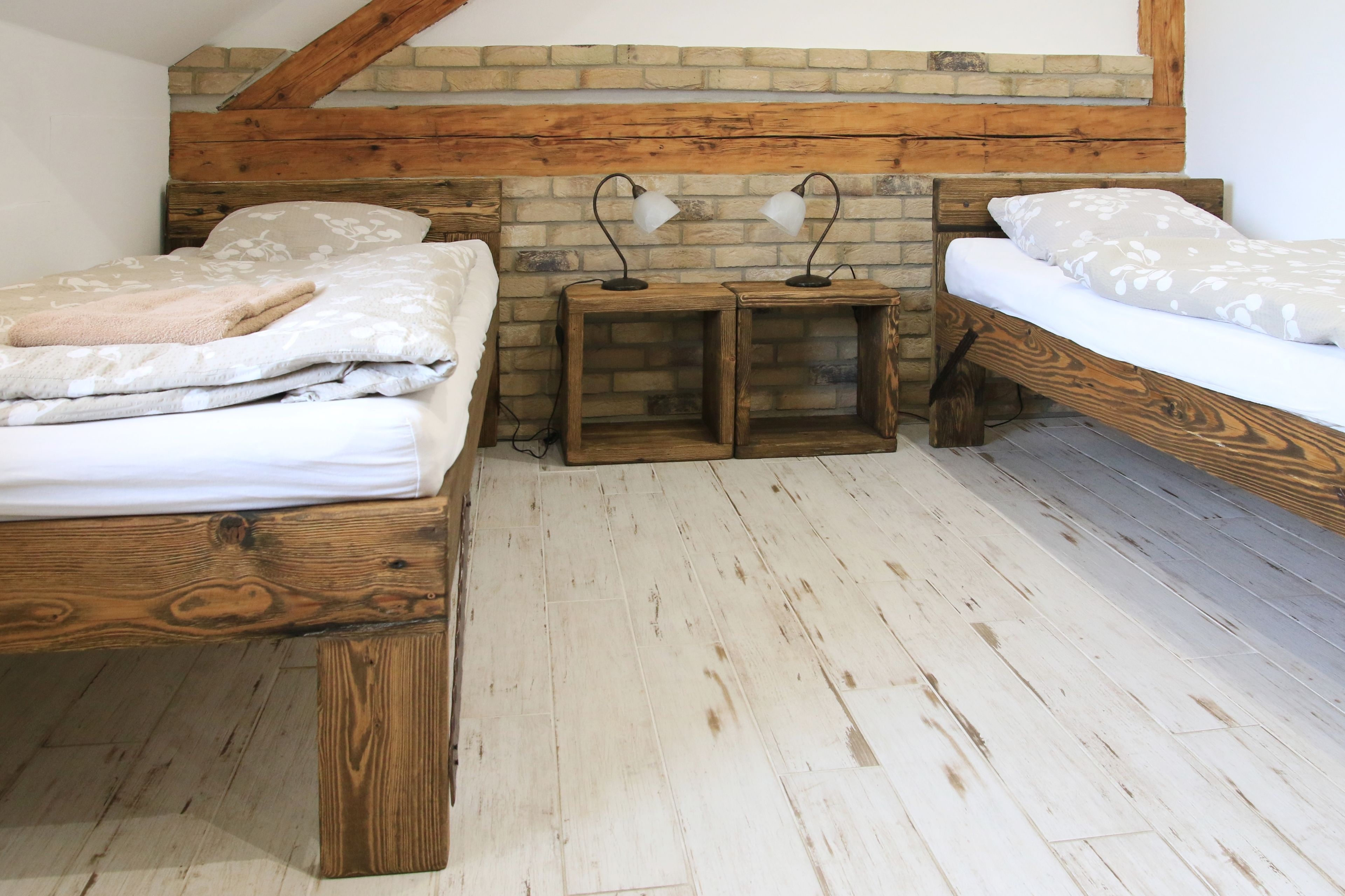 A bedroom with two wooden beds, a brick wall, and a wooden floor.