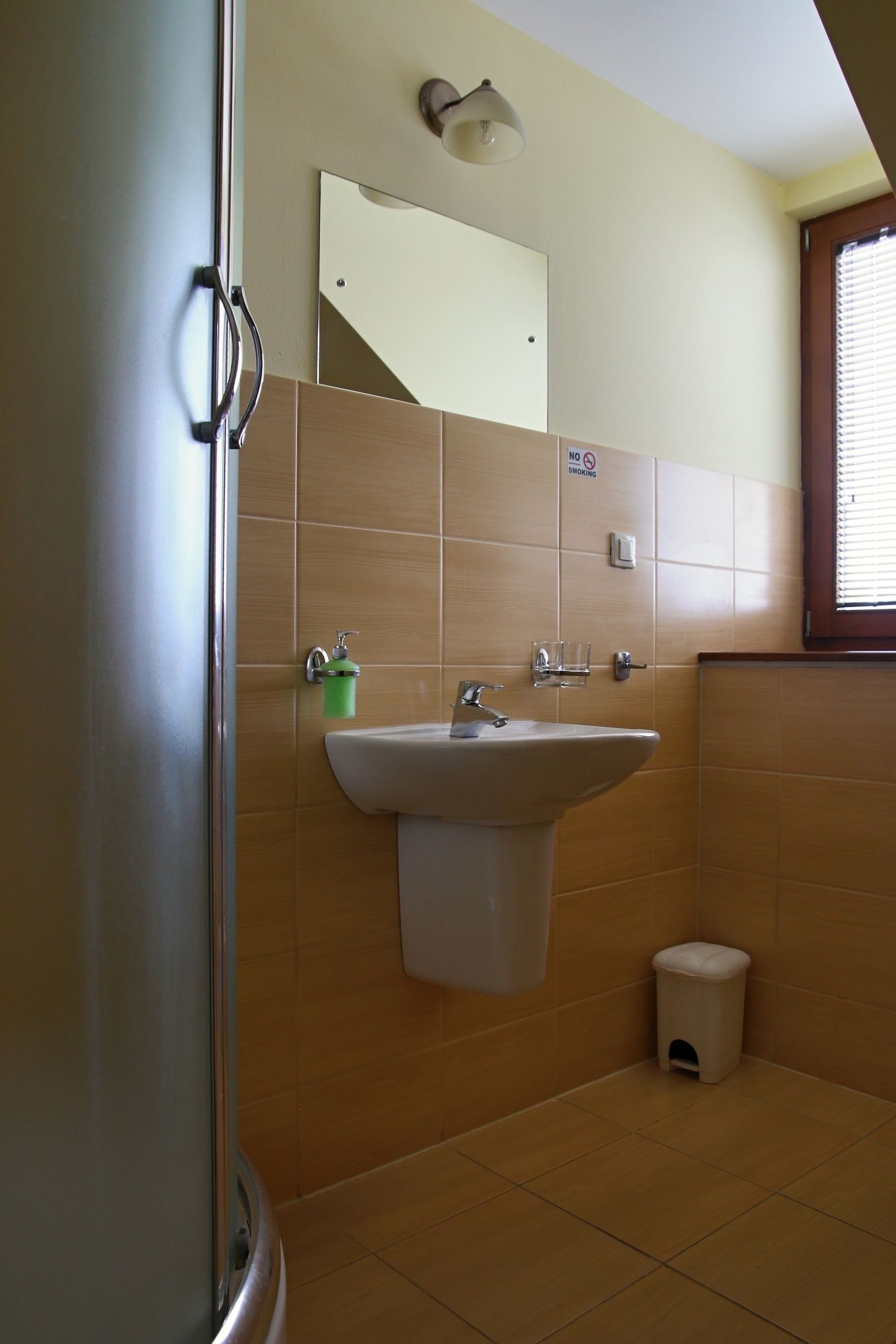 Een badkamer met een wastafel, spiegel en een vuilnisbak.