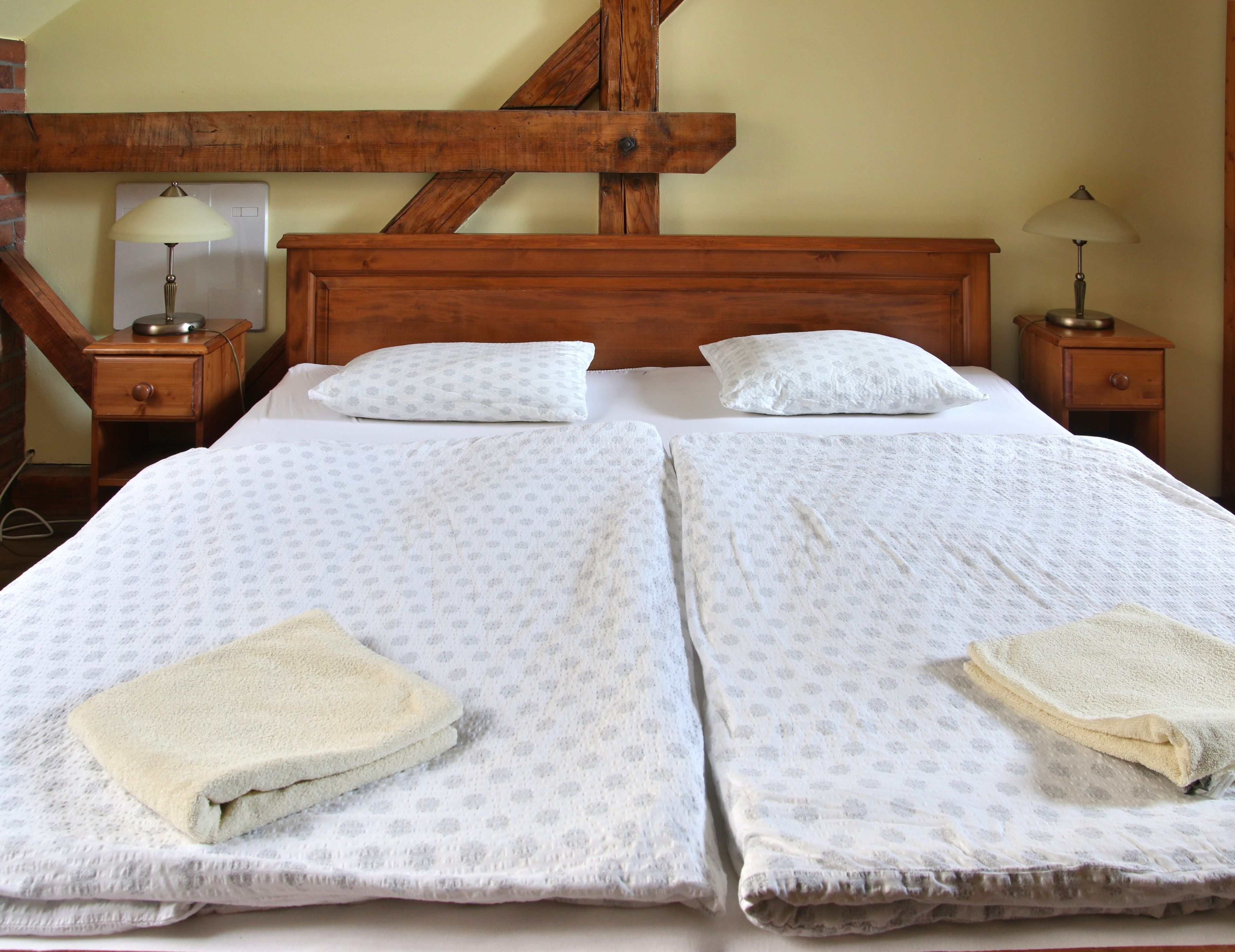A double bed with two pillows, a wooden headboard, bedside tables with lamps, and a wall-mounted heater.