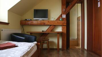 Un dormitorio con cama, escritorio, silla, televisor y puerta al baño.