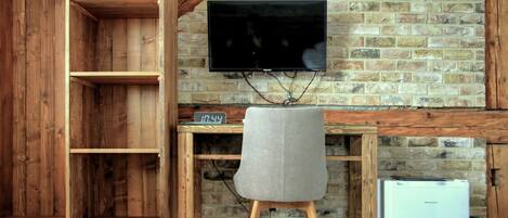 Un escritorio de madera con un televisor, una silla gris y un refrigerador blanco.