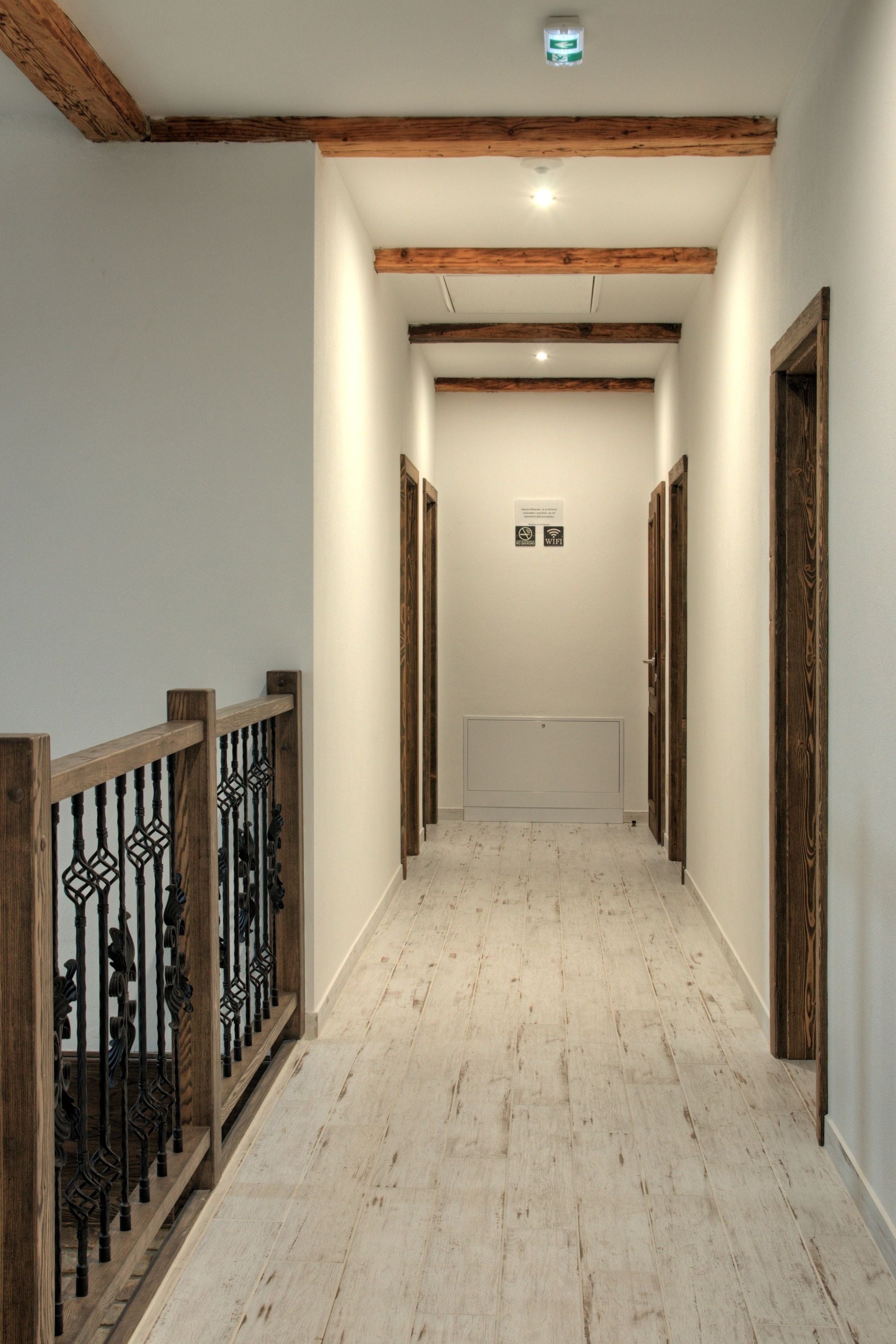 Un pasillo con vigas de madera, suelo blanco y una puerta al final.