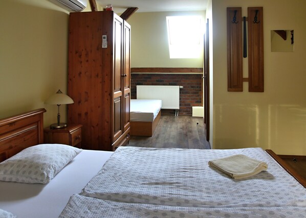 A bedroom with a wooden wardrobe, a bed with a white duvet, a bedside table with a lamp, and a brick wall with a radiator. - Penzion pri Mlyne (Nitra)