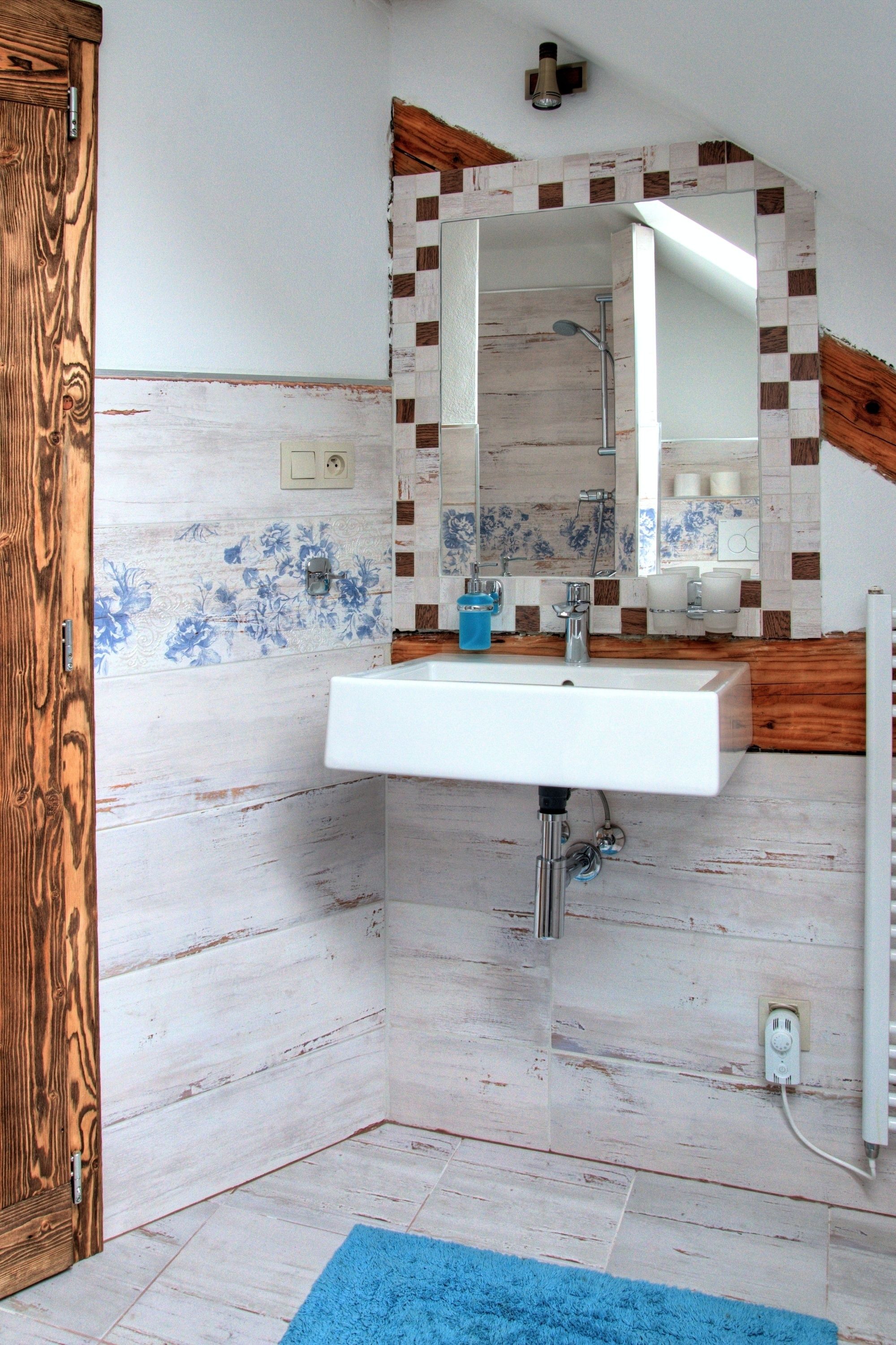 A bathroom with a wooden door, a white sink, a mirror, and a blue rug.