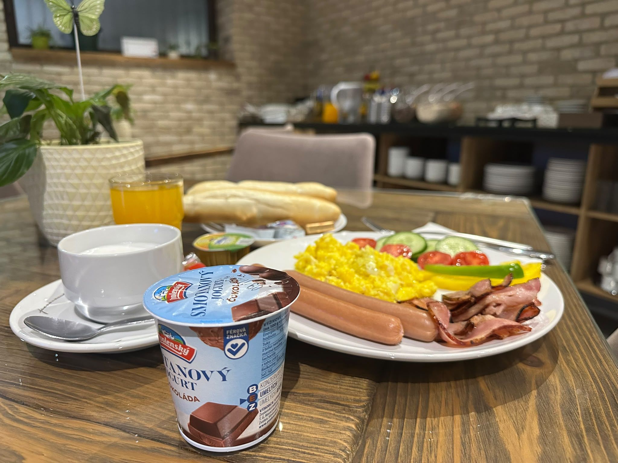 A breakfast setting with a plate of eggs, bacon, and vegetables, a glass of orange juice, and a bowl of yogurt.