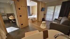 A modern hotel room with a wooden floor, a large bed, a sofa, a TV, and a bathroom with a bathtub. - Hotel Valtellina (Livigno)