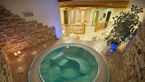 A hot tub in a stone-walled indoor area with a wooden staircase and a view of a room with a sofa and a plant. - Hotel Valtellina (Livigno)