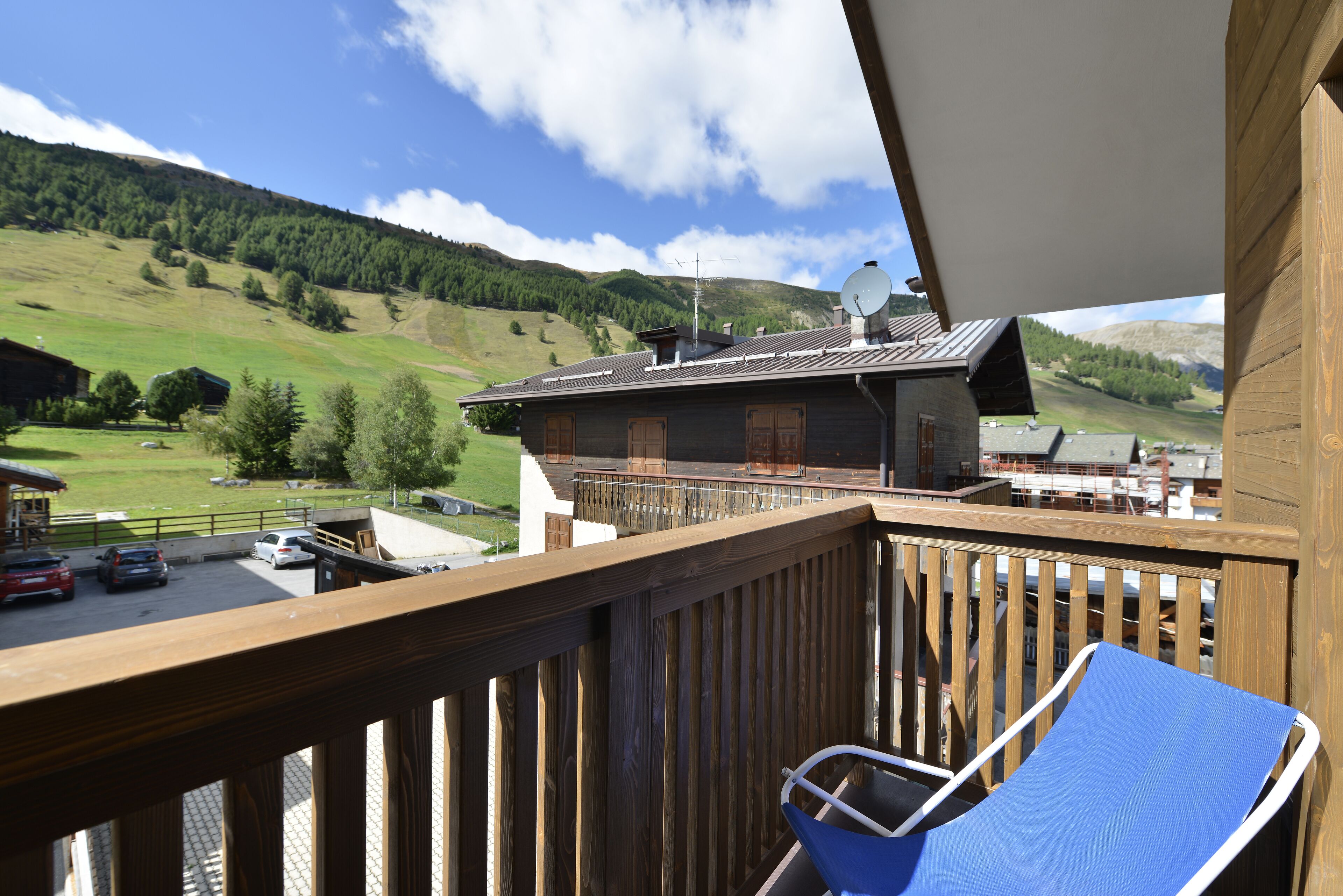 A balcony with a blue chair, a wooden deck, and a view of a mountain and a building with a sloped roof.