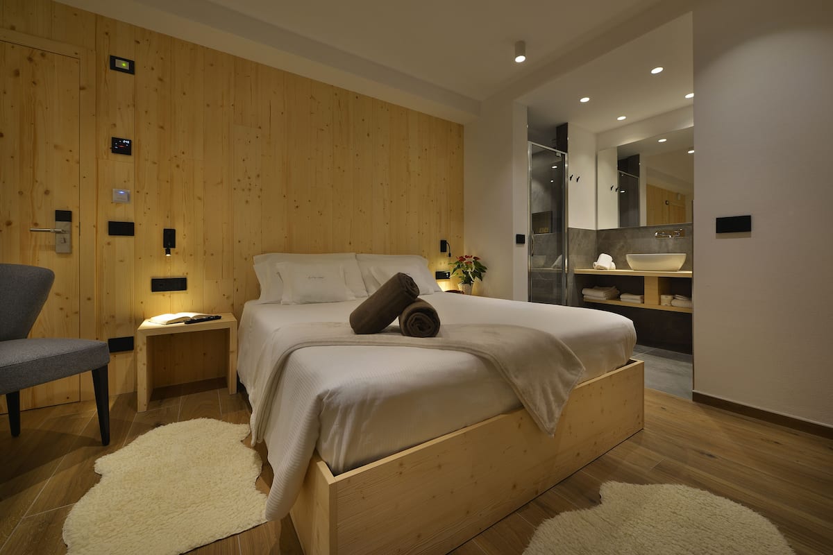 A modern bedroom with a wooden bed, a nightstand, a chair, and a bathroom visible through an open door.