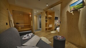 A modern room with a grey sofa, wooden walls, a television, and a wooden cabinet with towels. - Hotel Valtellina (Livigno)