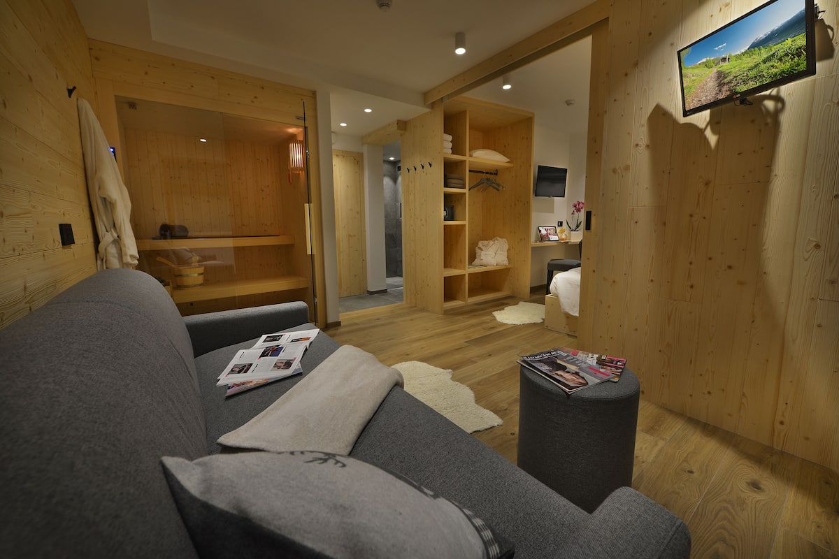 A modern room with a grey sofa, wooden walls, a television, and a wooden cabinet with towels.
