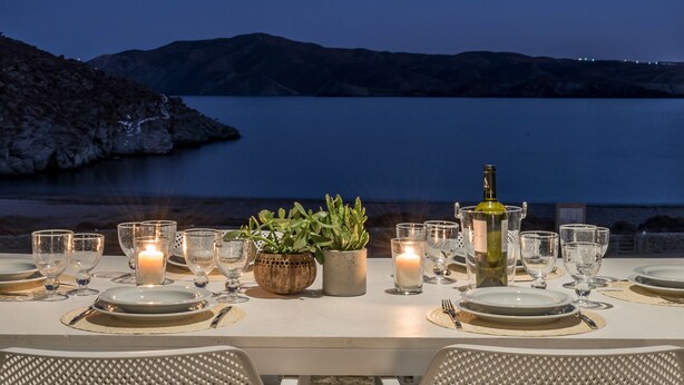 A table set for dining with a view of a lake and mountains at dusk. - Eneos Kythnos Beach Villas (Kithnos)