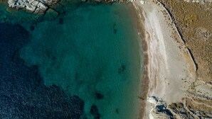 An aerial view of a coastal area with clear turquoise waters, rocky terrain, and a sandy beach. - Eneos Kythnos Beach Villas (Kithnos)