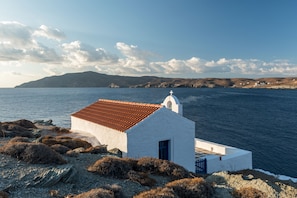 A small white building with a red-tiled roof by the sea, surrounded by rocky terrain and sparse vegetation. - Eneos Kythnos Beach Villas (Kithnos)