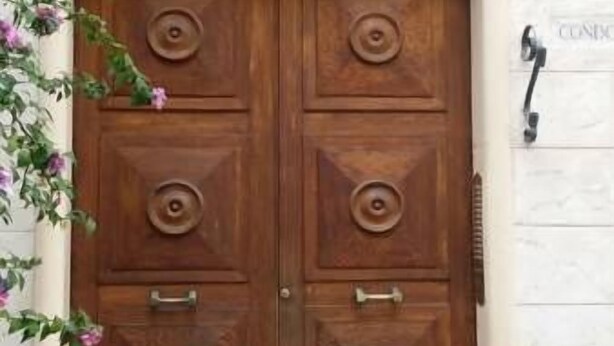 A double wooden door with a brass handle and a brass door knocker, set in a beige wall with a number '30' visible. - Casa Rosy (Rome)