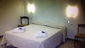 A single bed with a white bedspread and two folded towels, a wooden chair, and a wall-mounted light fixture. - Casa Rosy (Rome)