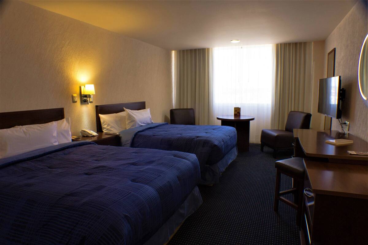 A hotel room with two beds, a desk, a chair, a TV, and a small table.