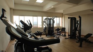 Ein Fitnessstudio mit Trainingsgeräten, großen Fenstern und hoher Decke.