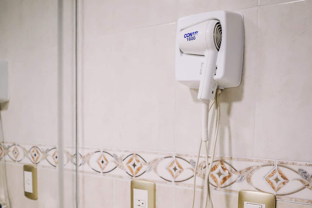 A bathroom with a hairdryer mounted on the wall, a towel dispenser, and a box of tissues on the counter.
