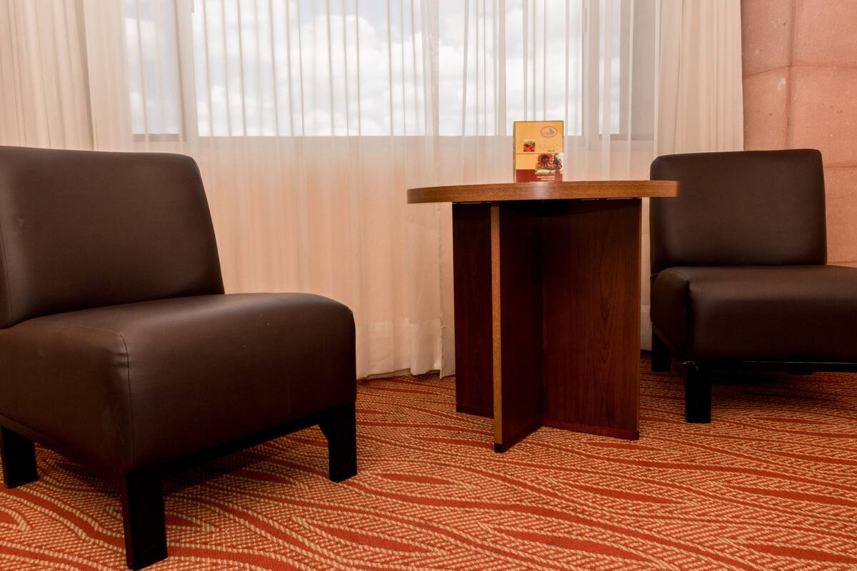 A hotel room with two brown leather armchairs, a wooden side table, and a patterned carpet.