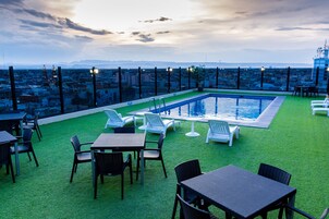 A rooftop pool area with artificial grass, lounge chairs, and tables.