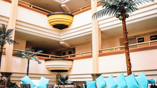 Ein Hotelatrium mit mehreren Etagen, einer zentralen Palme und Sitzbereichen mit blauen Kissen.