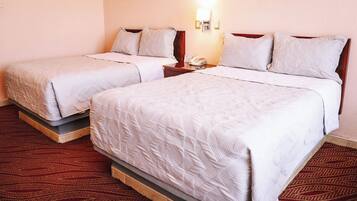 A hotel room with two beds, a nightstand with a phone, and a wall-mounted light fixture.